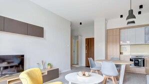 A modern living room with a TV, yellow armchair, and a dining area with a table and chairs. - Bright Apartment | River View and Parking Lot (Gdańsk)