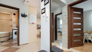 A modern apartment with a kitchen, a living area, and a bathroom. There is a washing machine in the kitchen, a mirror in the living area, and a door with a glass panel.