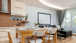 A modern kitchen with white cabinets, a wooden dining table set for four, and a black sofa in the living area.