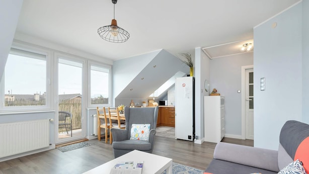 A modern living room with a white sofa, a grey armchair, and a white coffee table. There is a large window providing natural light, and a view of the outside.