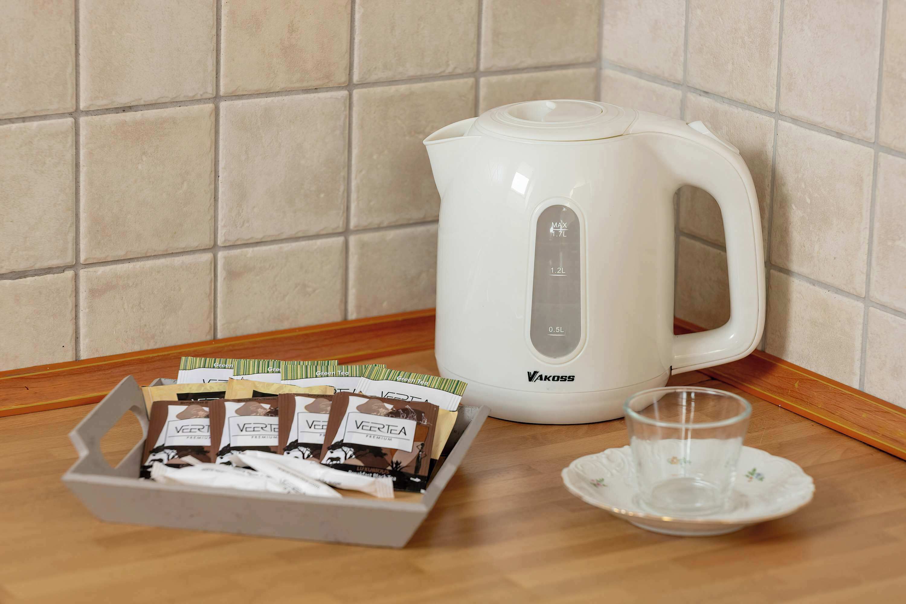 A white electric kettle, a glass cup, and a box of coffee pods on a wooden countertop.