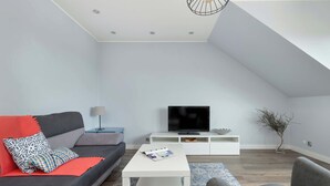 A modern living room with a grey sofa, a white coffee table, and a flat-screen TV on a white stand.