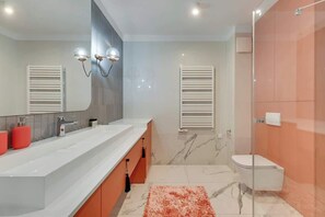 Un bany modern amb un mirall gran, dues làmpades penjades a la paret, un lavabo blanc, un vàter i una cabina de dutxa de vidre.