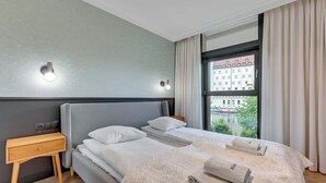 Habitación de hotel con cama, dos mesitas de noche, una ventana con cortinas y vistas a edificios.