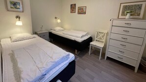 Un dormitorio con dos camas, una silla, un aparador y lámparas fijadas a la pared.