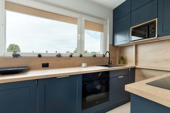 A modern kitchen with dark cabinets, a wooden countertop, a built-in oven, and a microwave.
