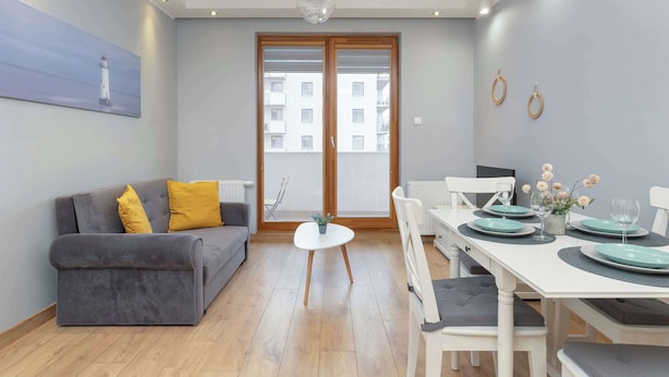 Een moderne woonkamer met een grijze bank, een klein wit tafeltje en een eethoek met een witte tafel voor vier personen.