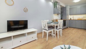 Een moderne keuken met grijze kastjes, een witte eettafel en een flatscreen televisie op een witte standaard.