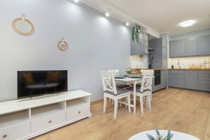 A modern kitchen with grey cabinets, a white dining table, and a flat-screen TV on a white stand.