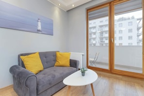 A modern living room with a grey sofa, two yellow cushions, a white coffee table, and a painting of a lighthouse on the wall.