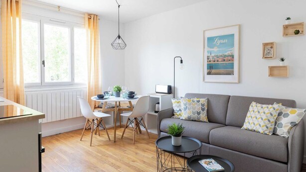A modern living room with a grey sofa, a dining table with chairs, a small kitchen area, and a window with curtains. - Dify City - Charpennes (Villeurbanne)