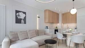 Una sala de estar moderna con un sofá seccional, una mesa de comedor con sillas, y un área de cocina con armarios de madera y salpicadero de mármol.