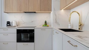 Una cocina moderna con armarios blancos, un horno negro, una cocina a gas de acero inoxidable, un grifo dorado y una encimera de mármol.