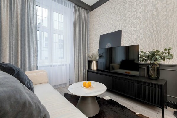 Uma sala de estar moderna com um sofá, uma mesa de centro redonda com frutas, uma TV e uma parede estampada.