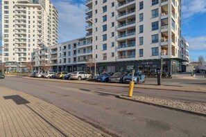 Um edifício moderno de vários andares, com varandas, entrada coberta e área de estacionamento com vários carros.