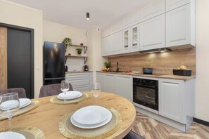 A modern kitchen with white cabinets, a built-in oven, and a dining area with a round table set for four. - Elegant Apartment for 6 Persons | Parking | Patio (Gdańsk)