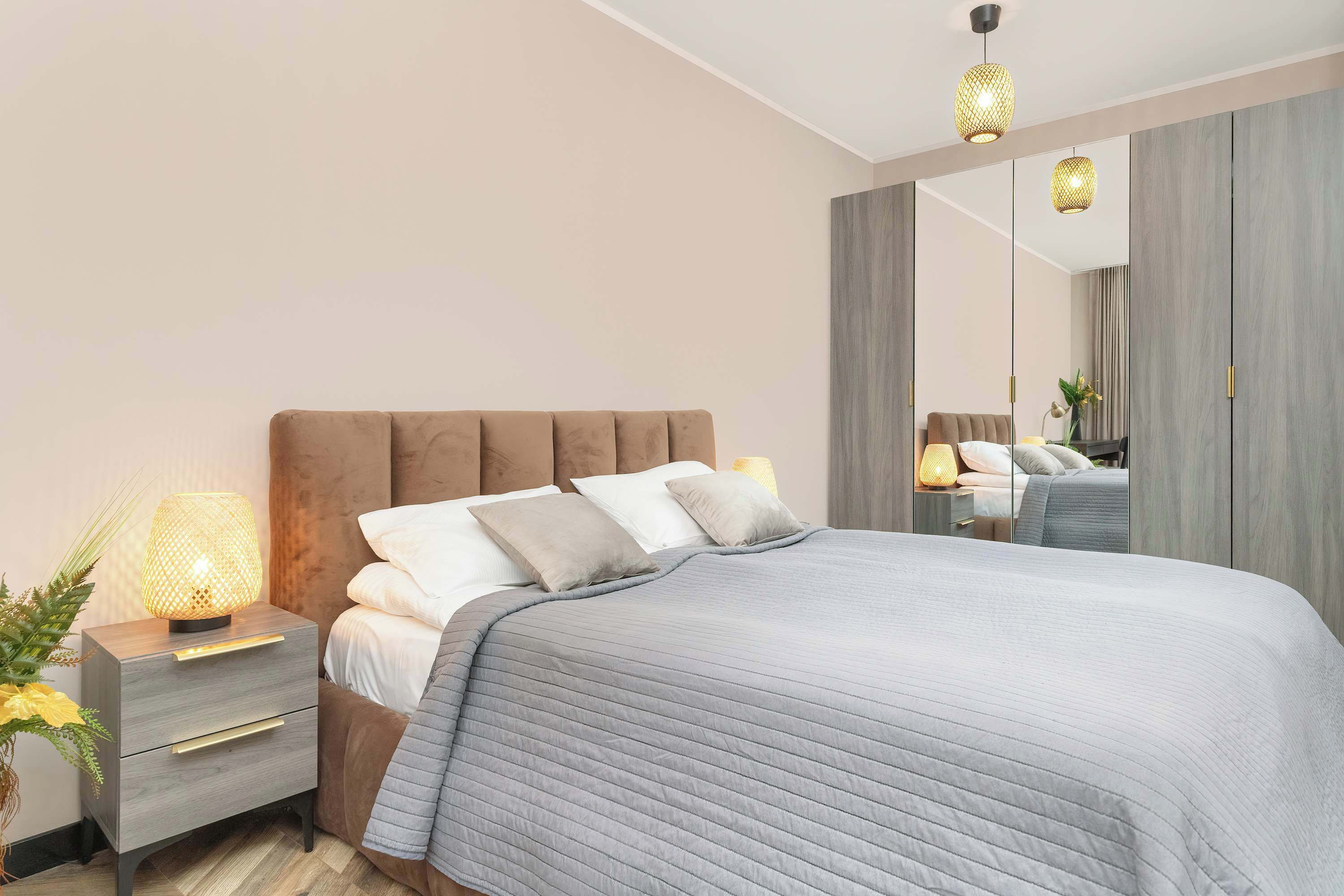 A modern bedroom with a large bed, a bedside table with a lamp, and a mirror on the wall.