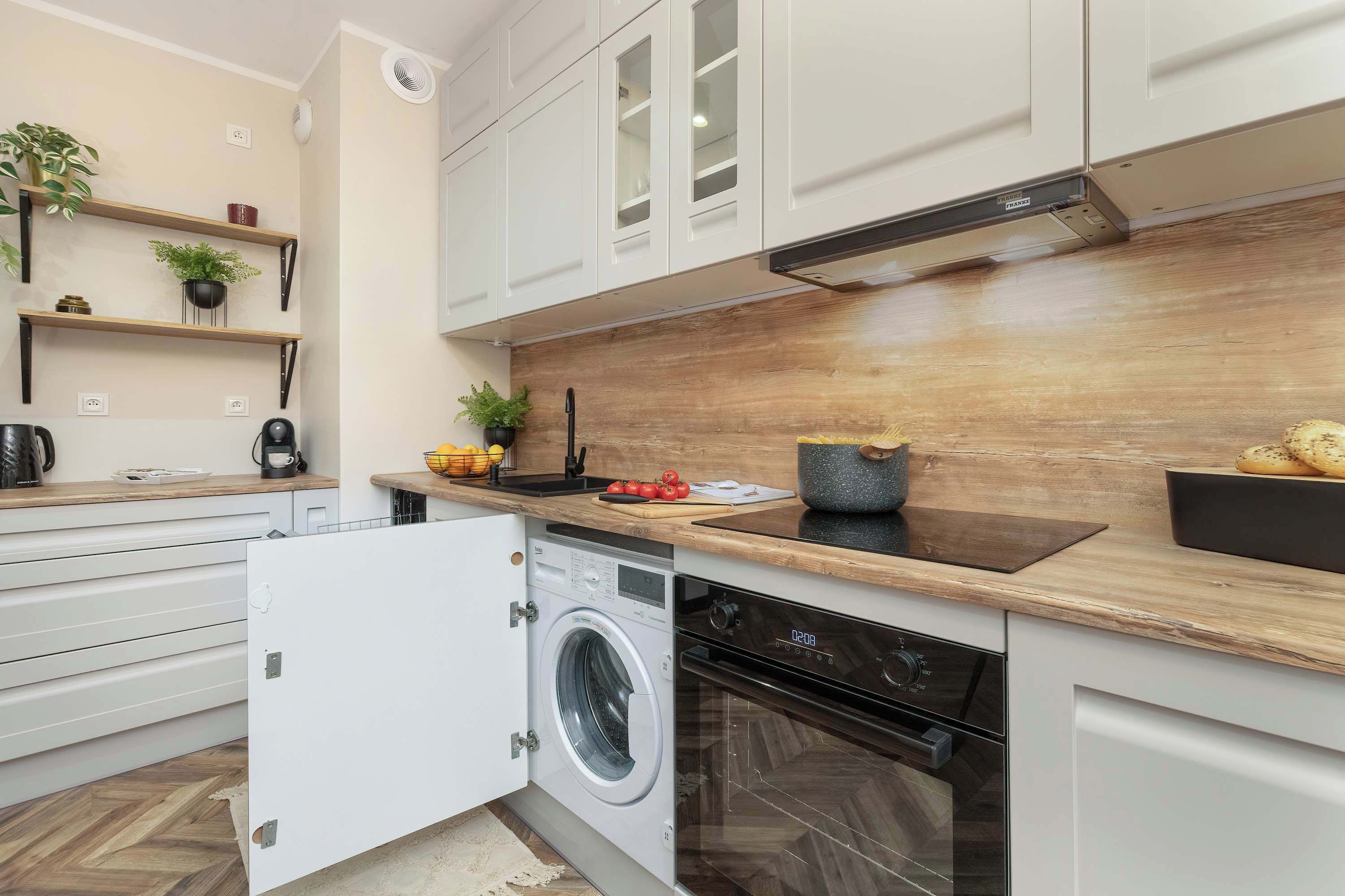 A modern kitchen with white cabinets, a wooden countertop, a built-in washing machine, and a stove.