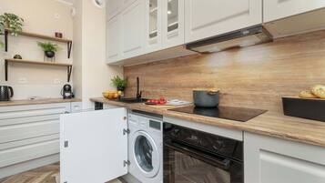 A modern kitchen with white cabinets, a wooden countertop, a built-in washing machine, and a stove.