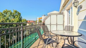 Ein Balkon mit Glastrennwand, Metallstühlen und einem kleinen runden Tisch.