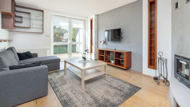 Ein modernes Wohnzimmer mit einer grauen Couch, einem Holztisch und einem an einer grauen Ziegelwand befestigten Fernseher.