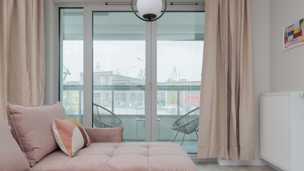 Una sala de estar moderna con un sofá rosa, una mesita con una taza, y vista a la ciudad a través de amplios ventanales.
