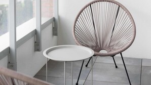 Una habitación moderna con una silla redonda de mimbre y una mesita blanca.