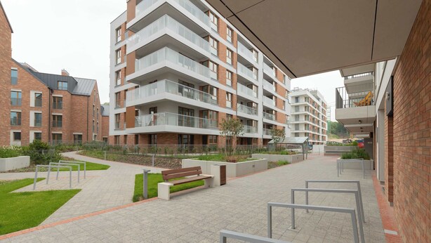 A modern apartment building with multiple balconies, a paved courtyard, and a bench.