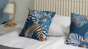A bed with white linens and two decorative pillows with a leaf pattern.