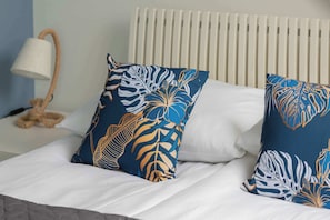 Un lit avec du linge de lit blanc et deux coussins décoratifs ornés d’un motif de feuilles.