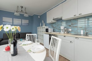 Une cuisine moderne avec des meubles blancs, un pare-feu bleu et un coin repas avec une table blanche mise pour deux personnes.