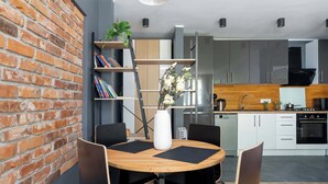Una cocina moderna con gabinetes blancos, una pared decorativa de ladrillo y un comedor con mesa de madera y sillas negras.