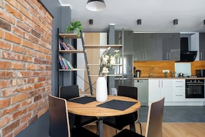 Una cucina moderna con mobili bianchi, una parete decorata con mattoni e un'area pranzo con tavolo in legno e sedie nere.