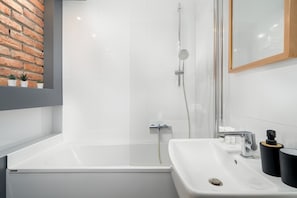 Un baño moderno con ducha envuelta en vidrio, una bañera blanca y un lavamanos con artículos de aseo.