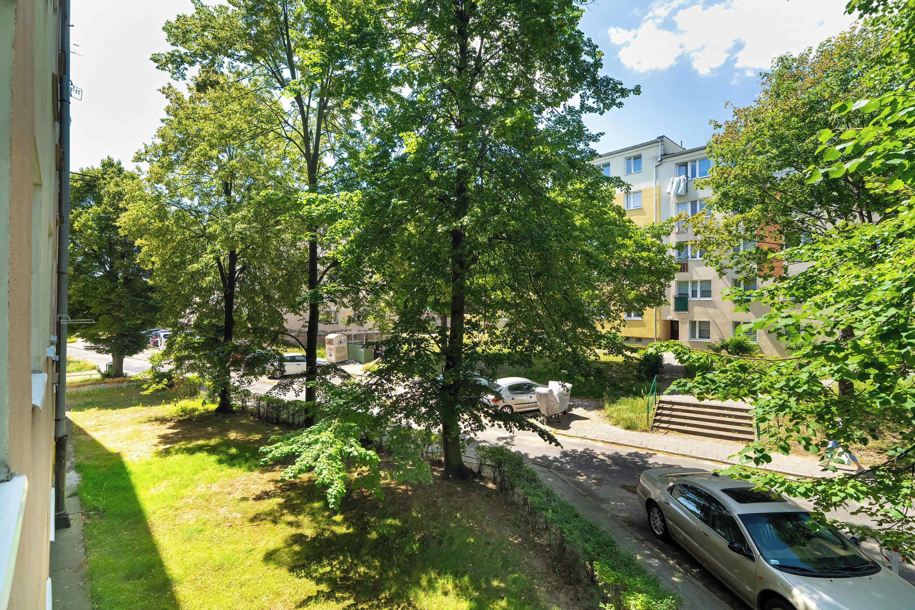Un quartier résidentiel avec une voiture garée, une rue bordée d’arbres et un immeuble doté de balcons.