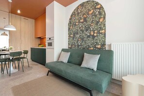 Un soggiorno moderno con un divano verde, zona pranzo, cucina e un ampio murale a tema frutta.