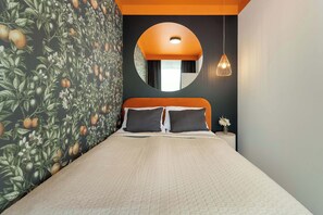Un letto con copriletto trapuntato, uno specchio rotondo sopra e una parete decorata con un motivo a frutta.