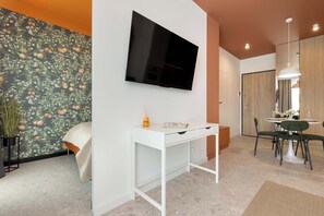 Une chambre moderne dotée d’un téléviseur à écran plat, d’un bureau blanc, d’une table à manger avec des chaises et d’un mur orné d’un motif.