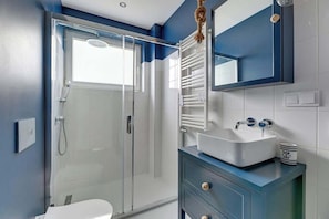 A modern bathroom with a glass shower enclosure, a white sink, and a blue vanity. - Comfortable Apartment | Close to the Center | Pet Friendly (Gdańsk)