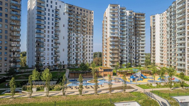 Un ensemble résidentiel composé d’immeubles d’habitation à étages élevés, d’une cour centrale avec des jeux pour enfants et d’espaces verts environnants.