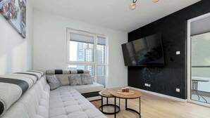 Un salon moderne avec un canapé d’angle, une petite table ronde et un téléviseur à écran plat fixé sur un mur noir.