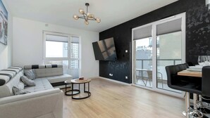 Un salon moderne avec un canapé d’angle gris, une table basse ronde et un coin repas avec une chaise noire.