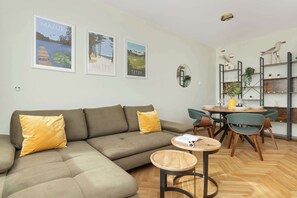 Una sala de estar moderna con un sofá modular, una mesa de comedor con sillas y una zona de cocina con estanterías y plantas.
