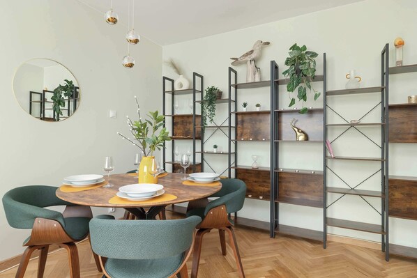 Un comedor con una mesa redonda de madera, sillas tapizadas en verde y un muro espejado.