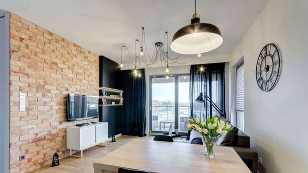 A modern living room with a brick wall, a flat-screen TV, a dining table, and a large window.