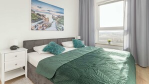 Une chambre à coucher avec un lit, une table de chevet, une fenêtre avec des rideaux et un tableau au mur.