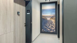 A hallway with a wooden door, a digital lock, and a view of a beach through a glass door.