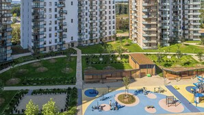 A high-rise residential building with multiple balconies, a playground, and landscaped areas.