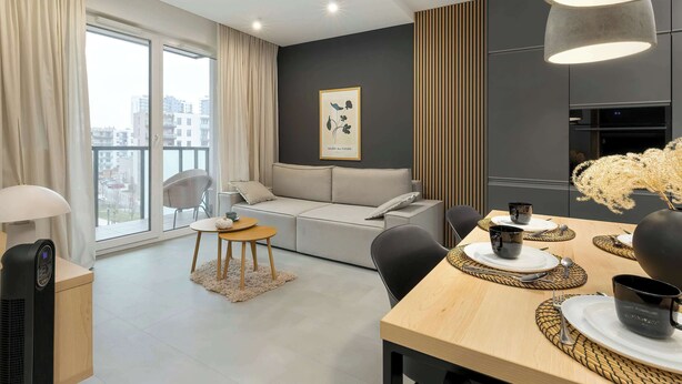 A modern living room with a sofa, dining table, and a large window with curtains.