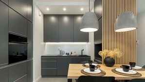 A modern kitchen with dark cabinets, a wooden dining table with black chairs, and pendant lights.
